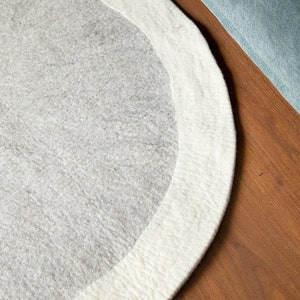 May include: A round, gray and white rug with a white border. The rug is made of a soft, fuzzy material.