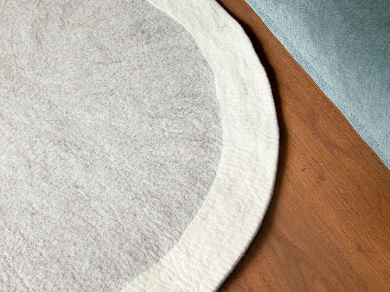 May include: A round, gray and white rug with a white border. The rug is made of a soft, fuzzy material.