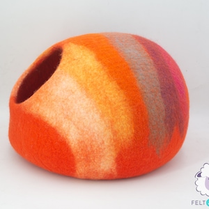 May include: Orange, yellow, pink and grey felted wool cat bed. The bed is shaped like a dome with a large opening on one side.