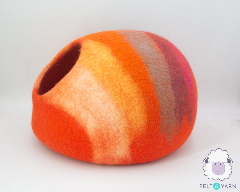 May include: Orange, yellow, pink and grey felted wool cat bed. The bed is shaped like a dome with a large opening on one side.