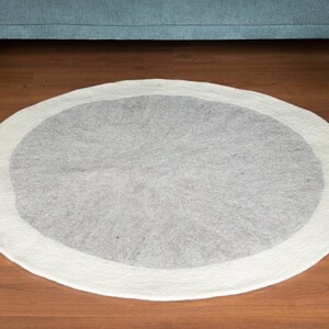 May include: A round, white and gray area rug with a white border. The rug is made of wool and has a soft, fluffy texture.