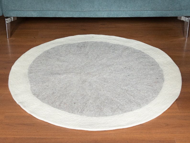 May include: A round, white and gray area rug with a white border. The rug is made of wool and has a soft, fluffy texture.