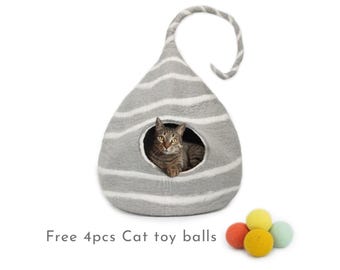 Puede incluir: Una cama para gatos gris y blanca a rayas con forma de lágrima con un gato dentro. La cama tiene una pequeña abertura para que el gato pueda entrar. La cama viene acompañada de cuatro bolas de fieltro de colores. Gratis 4pcs Cat toy balls.