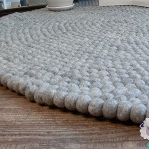 K&ouml;nnte beinhalten: Ein runder grauer Filzteppich aus kleinen, runden Kugeln. Der Teppich liegt auf einem Holzboden.