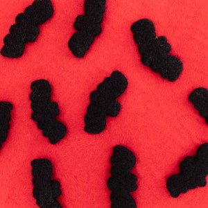 May include: A red felt background with ten black felt bats scattered across the surface.