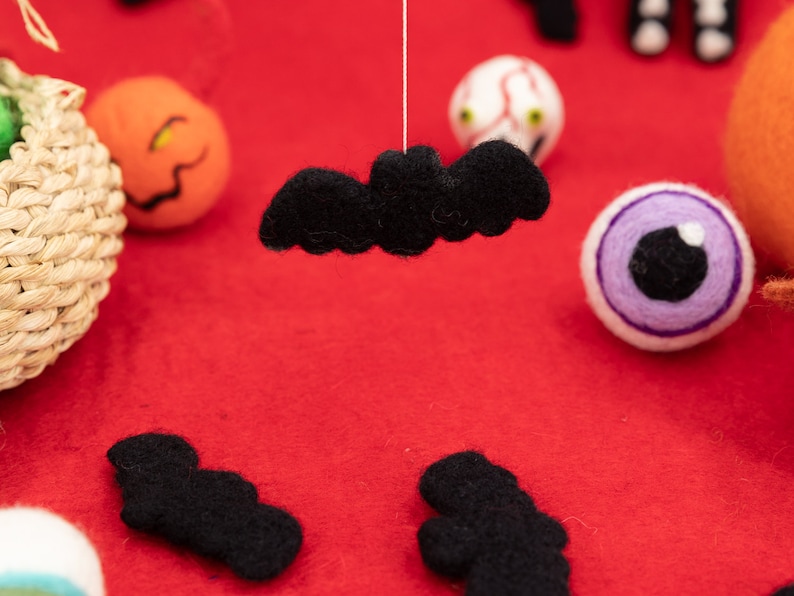 May include: A collection of felt Halloween decorations, including a black bat, a purple eye, and a pumpkin. The decorations are on a red felt background.