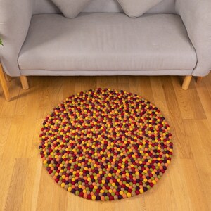 May include: A round, multi-colored felt rug made of small balls. The rug is in shades of red, orange, yellow, green, and purple.
