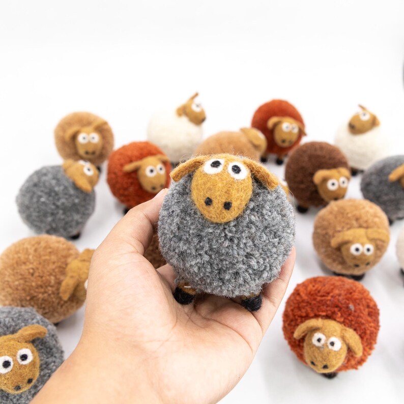 May include: A collection of felt sheep in various colors, including brown, gray, and orange. The sheep are all handmade and have a fluffy texture. They are arranged in a circle on a white background.