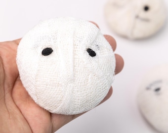 May include: A white gauze ball with two black eyes, resembling a ghost. The ball is being held in a hand.