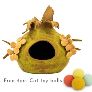 May include: A green felt cat bed shaped like a house with a brown felt roof and yellow felt flowers. The bed has a round opening for the cat to enter. The image includes the text "Free 4pcs Cat toy balls". Four colourful felt balls are shown in the lower right corner of the image.