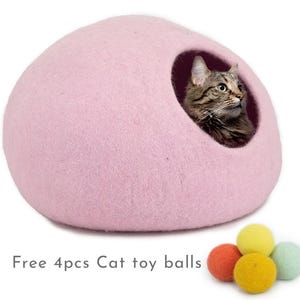 May include: A pink felt cat bed shaped like a dome with a cat peeking out of the opening. The bed comes with four colourful felt cat toy balls.