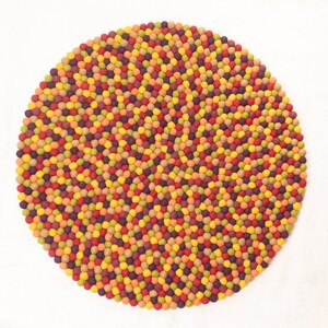 May include: A round, colorful rug made of felt balls in shades of red, orange, yellow, green, and purple. The balls are arranged in a spiral pattern.