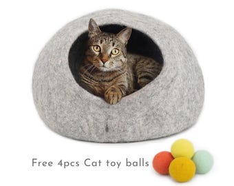 May include: A grey felt cat bed shaped like a dome with a cat inside. The bed has a dark grey opening for the cat to enter. The image includes the text "Free 4pcs Cat toy balls" and shows four colourful felt balls.