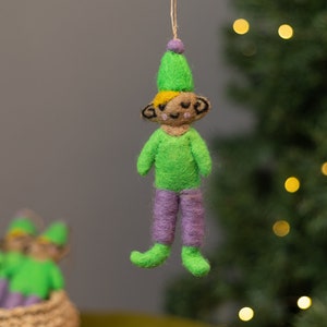 Op de afbeelding: Groene vilten elfen ornament met een paars vilten lichaam en een gele vilten hoed. De elf heeft een glimlachend gezicht met zwarte ogen en een zwarte mond.