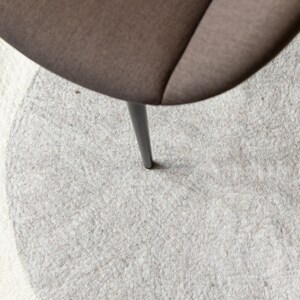 May include: A gray and white round rug with a single black chair leg in the center.