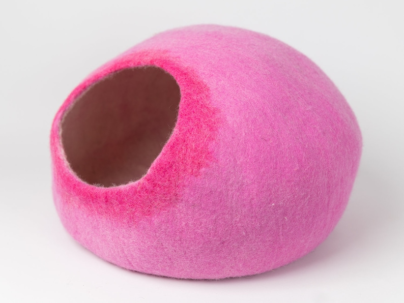 May include: A pink felt cat bed shaped like a dome with a large opening for entry. The bed is made of soft, fuzzy felt and is perfect for small pets.