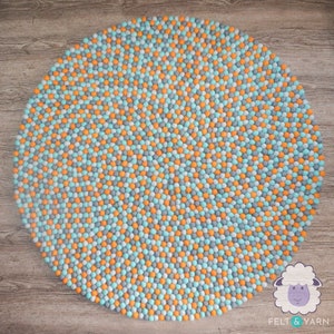 May include: A round felt rug with a pattern of small, colorful balls. The rug features a mix of orange, light blue, and gray balls. The rug is a decorative item for a home.