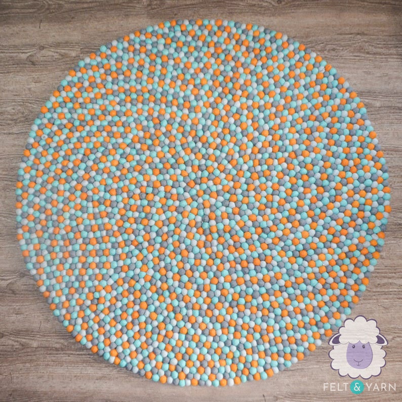 May include: A round felt rug with a pattern of small, colorful balls. The rug features a mix of orange, light blue, and gray balls. The rug is a decorative item for a home.
