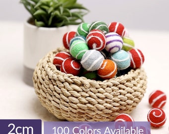 Könnte beinhalten: Ein Korb gefüllt mit bunten Filzkugeln, jede etwa 2 cm im Durchmesser. Die Kugeln sind in verschiedenen Farben und Mustern, darunter Rot, Grün, Blau und Weiß. 100 Farben verfügbar.