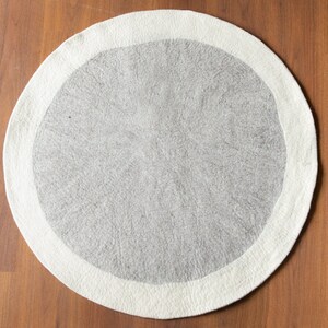 May include: A round, white and gray area rug with a white border. The rug is made of wool and has a soft, fluffy texture.