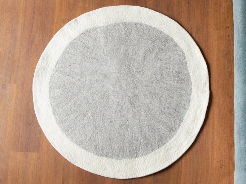 May include: A round, white and gray area rug with a white border. The rug is made of wool and has a soft, fluffy texture.