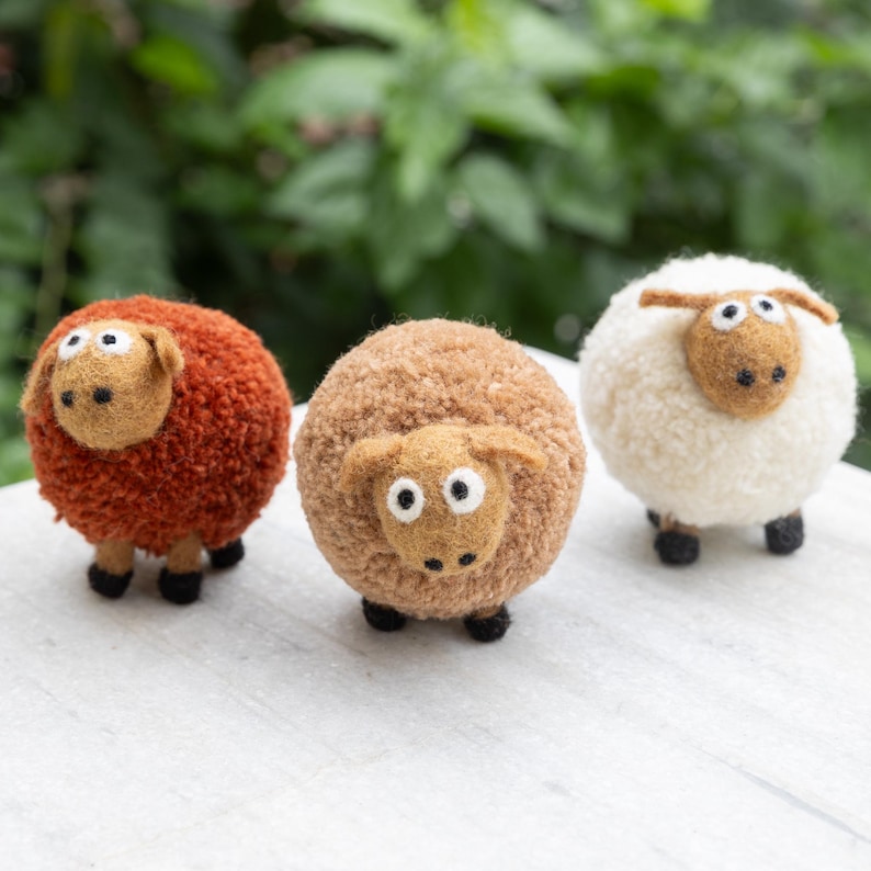 May include: Three felt sheep toys, one brown, one orange, and one white. The sheep have black eyes and black legs.