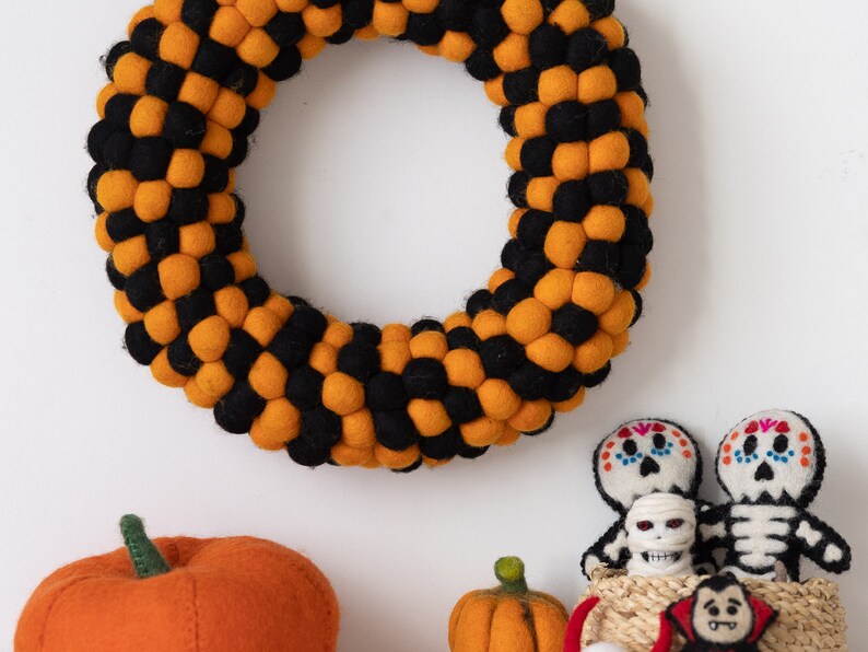 Puede incluir: Una corona de Halloween hecha de bolas de fieltro naranja y negro. Tambi&eacute;n hay dos esqueletos de fieltro, una calabaza de fieltro y un vampiro de fieltro.