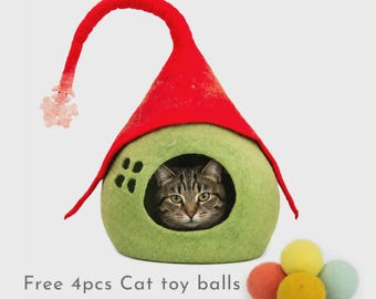 May include: A felted cat cave shaped like a pointed hat with a red top and a light green base featuring a small window cutout. A tabby cat is visible inside the opening. Four small, solid-colored felt balls are placed in front of the cave.