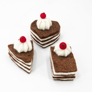May include: Three felt chocolate cakes with white frosting and red cherries on top. The cakes are in the shape of a heart and two squares.