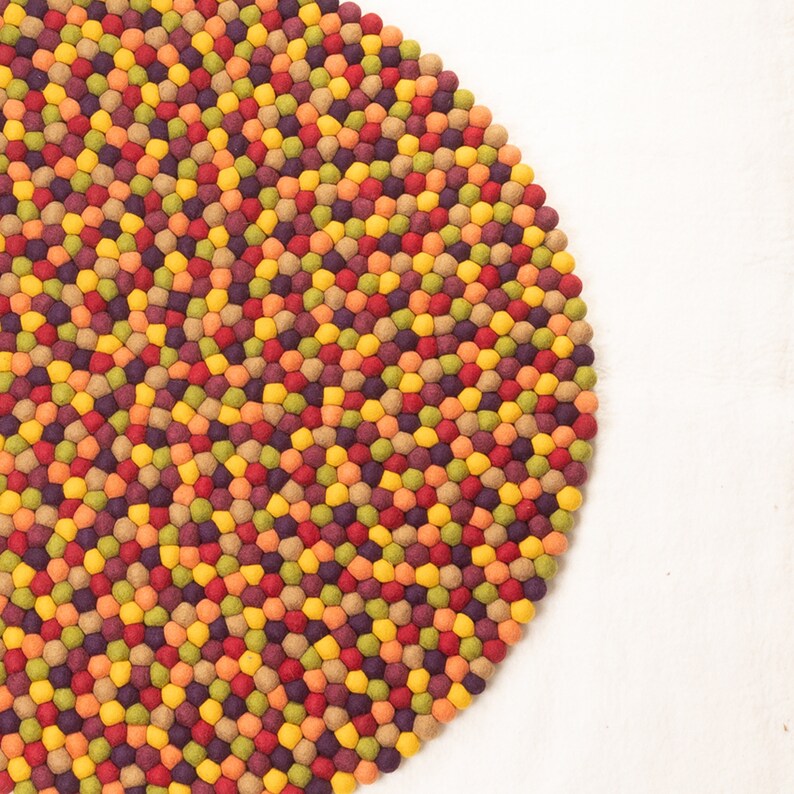 May include: A round, colorful rug made of felt balls. The rug is made up of small, densely packed balls in shades of red, orange, yellow, green, and purple.
