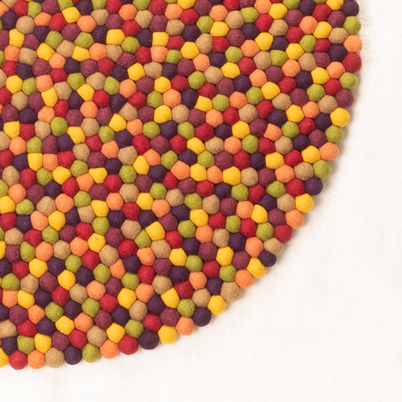 May include: A round, multi-colored felt rug with a pattern of small, round balls in shades of red, orange, yellow, green, and brown.