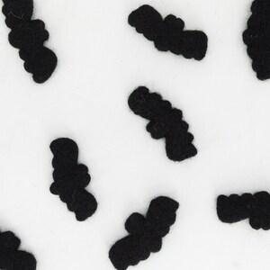 May include: A white background with multiple black felt bats scattered across the surface.