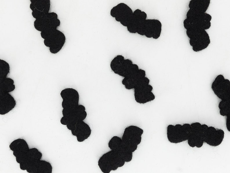 May include: A white background with multiple black felt bats scattered across the surface.