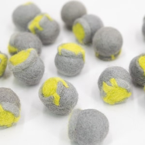 May include: A collection of gray felt balls with yellow accents. The balls are scattered on a white surface.
