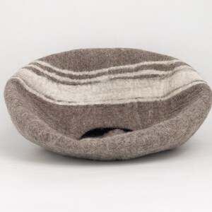 May include: A brown felt bowl with white stripes. The bowl is shaped like a half-sphere and has a hole in the bottom.