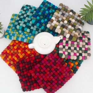 May include: Set of colorful felt pot holders in various shades of blue, green, orange, red, and pink. The pot holders are made of small, round felt balls woven together in a square shape.