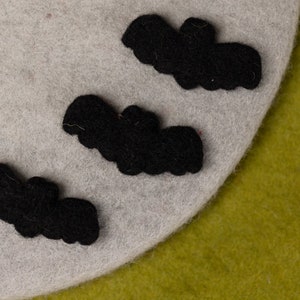 May include: Three black felt bats are arranged on a light gray felt background. The bats are different sizes and are all facing the same direction.