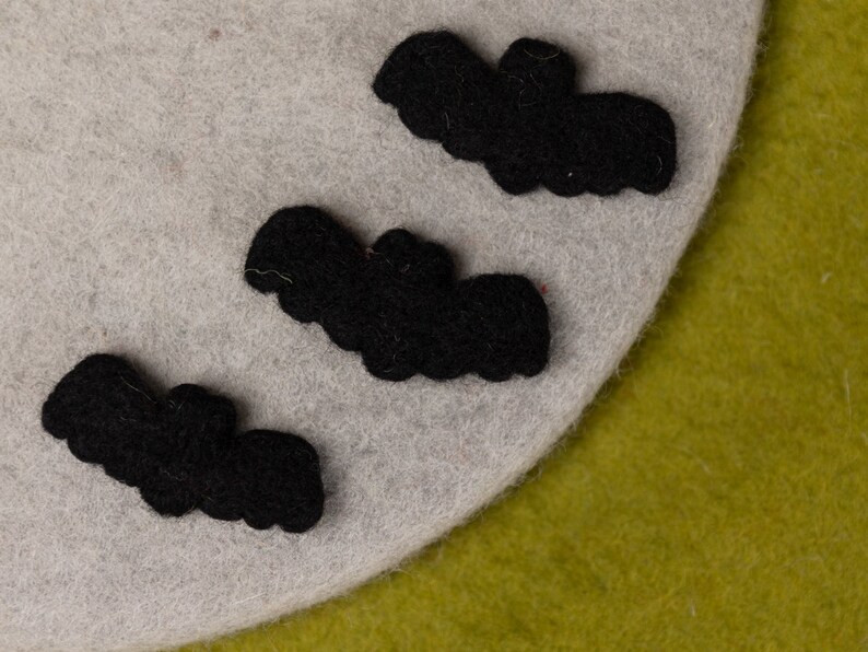 May include: Three black felt bats are arranged on a light gray felt background. The bats are different sizes and are all facing the same direction.