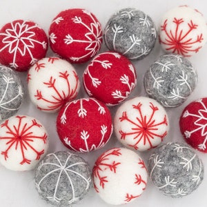 Peut inclure: Une collection d'ornements de Noël en feutre rouge, blanc et gris avec des motifs de flocons de neige.