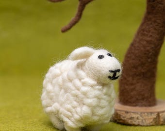 Pode incluir: Um brinquedo de ovelha de feltro branco com olhos pretos e nariz preto. A ovelha está em pé sobre uma superfície verde.