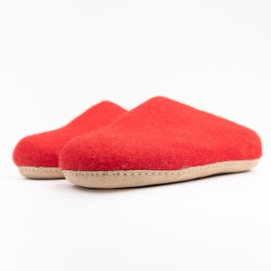 Könnte beinhalten: Ein Paar rote Filzpantoffeln mit einer hellbraunen Sohle. Die Pantoffeln sind weich und gemütlich, perfekt um die Füße im Winter warm zu halten.