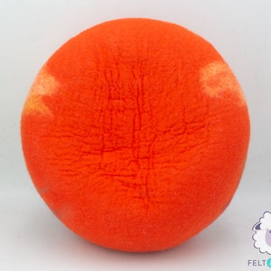 May include: A bright orange felted ball with a slightly lighter orange and yellow colour variation. The ball is made of wool and has a fuzzy texture.