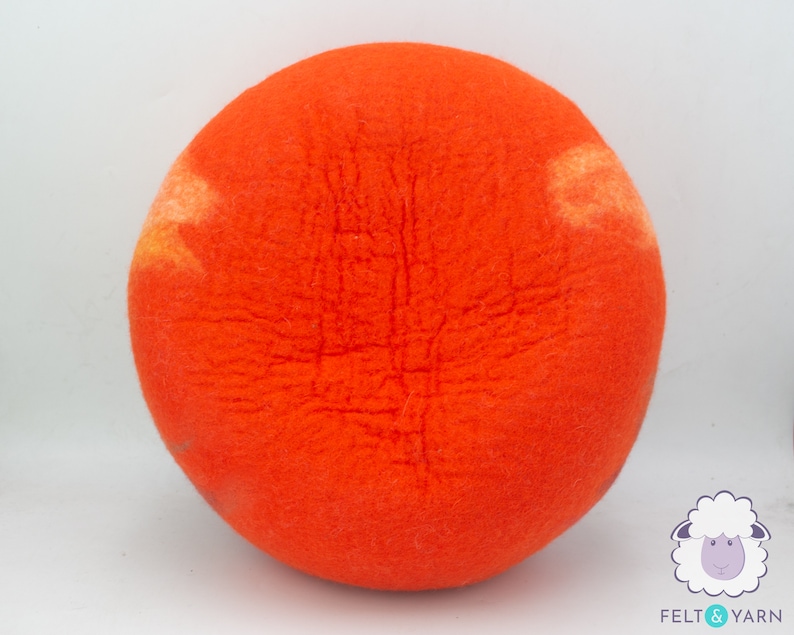 May include: A bright orange felted ball with a slightly lighter orange and yellow colour variation. The ball is made of wool and has a fuzzy texture.