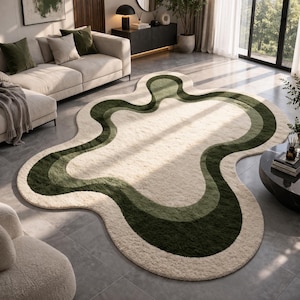 May include: A cream-colored, abstract-shaped rug with a wavy design in shades of green. The rug is placed on a tiled floor in a living room setting, with a sofa and other furniture visible in the background.