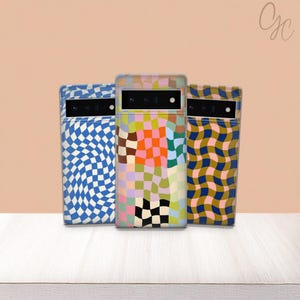 May include: Three phone cases with colorful, geometric patterns. The cases feature designs including blue and white wavy checkerboard, a patchwork of squares in various colors, and a gold and navy wavy pattern. The cases are displayed on a white surface.