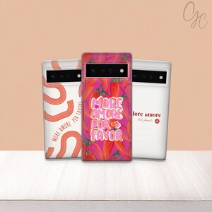 May include: Three phone cases with unique designs. The center case features a vibrant red chili pepper pattern with the text "MORE AMORE POR FAVOR." The other cases have white backgrounds with red text and designs. The cases are on a light peach background.