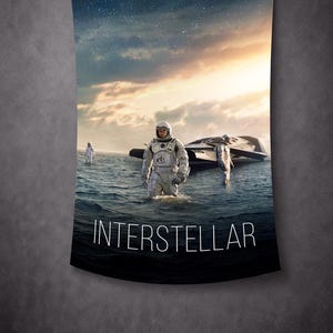 Op de afbeelding: Een wandtapijt met een scène uit de film "Interstellar". Astronauten in witte ruimtepakken staan in het water bij een ruimteschip. De titel "INTERSTELLAR" staat in witte tekst.