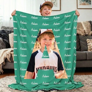 Könnte beinhalten: Eine türkisfarbene Decke mit dem Namen "Adam" in Weiß. Ein Foto eines lächelnden Kindes in Baseballuniform ist aus der Decke ausgeschnitten. Das Kind trägt eine Baseballkappe und das Wort "MUDHENS" ist sichtbar.