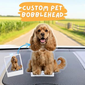May include: A custom pet bobblehead of a Cocker Spaniel dog, with a photo of the dog in a Polaroid-style frame. The bobblehead is light brown with long, floppy ears and a happy expression. The text "CUSTOM PET BOBBLEHEAD" is in an orange banner.