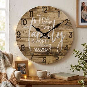 Puede incluir: Un reloj de pared redondo con diseño de tablones de madera. La esfera del reloj presenta números y manecillas negras, con las palabras "Time spent with family is worth every second" en escritura blanca. El reloj está en una pared clara.